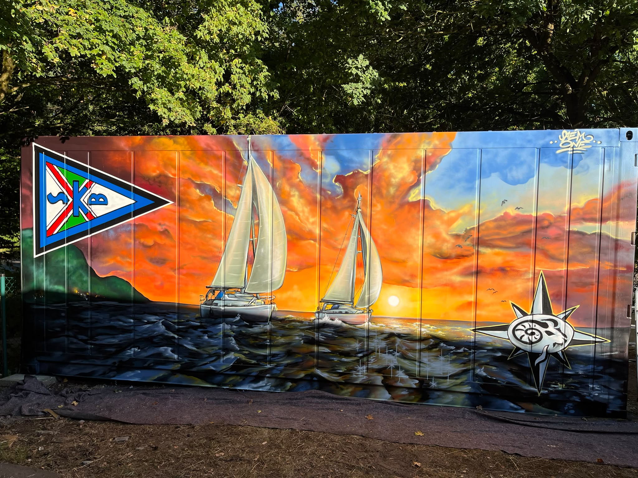 Bemalter Seecontainer am SKB-Seglertreff: Sonnenuntergang mit zwei Segelyachten und SKB-Stander